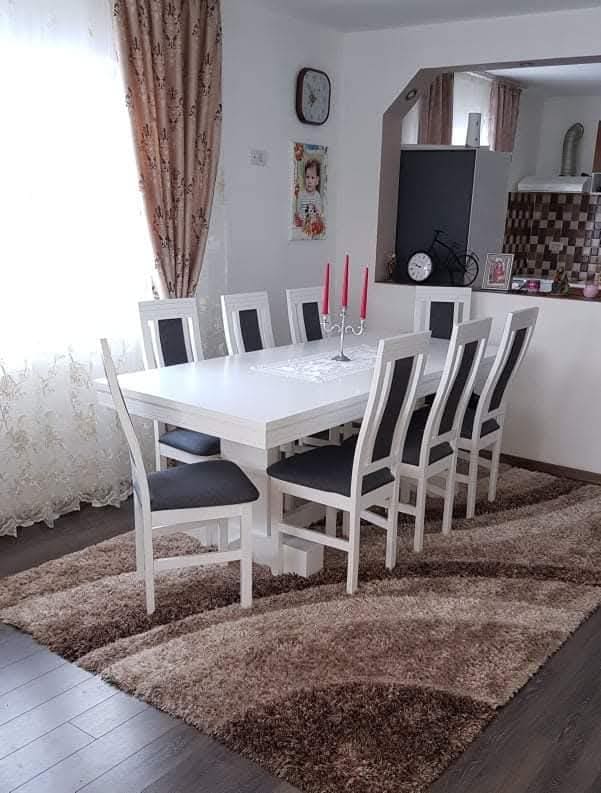 Masă albă cu scaune din lemn alb tapițate în gri închis, cu un sfeșnic cu trei lumânări roșii